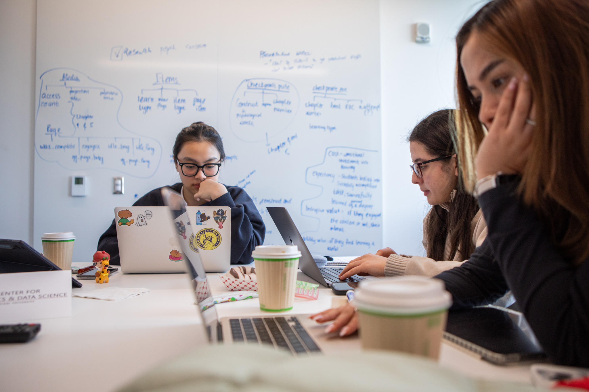 3 students sitting at a table working on their laptops.
