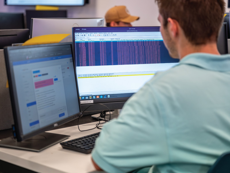 A student working on a information technology project with 2 monitor displays. 