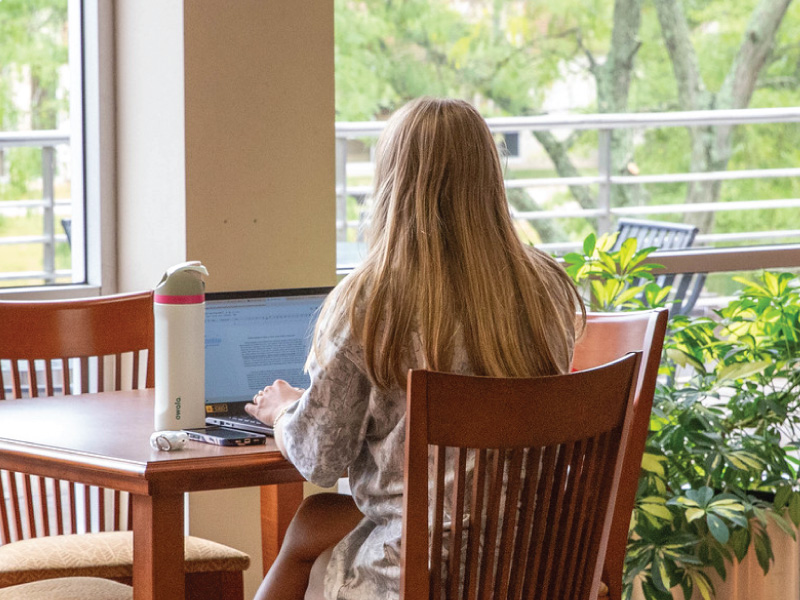 A student sitting at a table typing on her laptop.