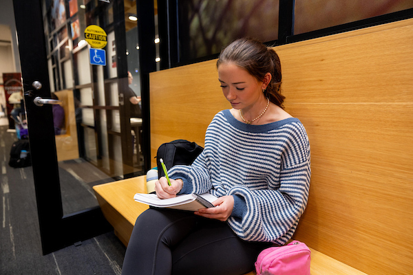 Student writing in a composition book outside of the Rinella Learning Center