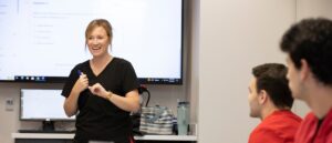 nursing professor in black scrubs speaking with class in lab