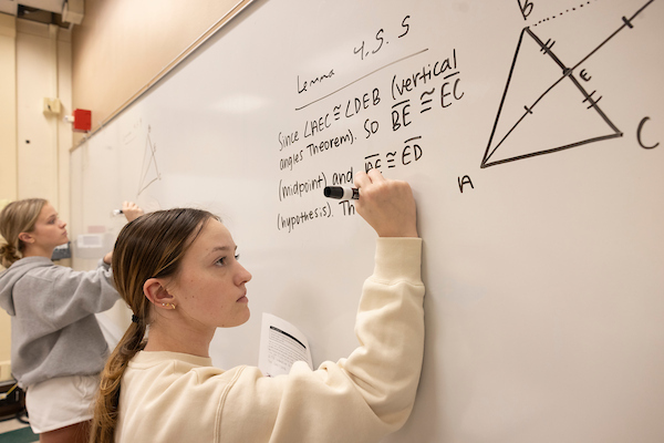 Student in Dr. Jason Gaddis' cloass working on a math problem at a white board.