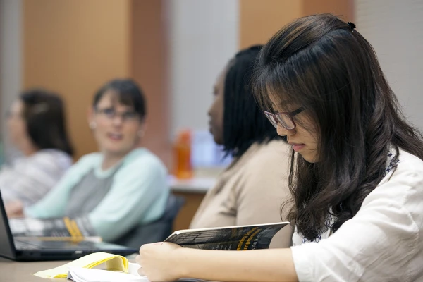 student sitting at desk with students discussing project