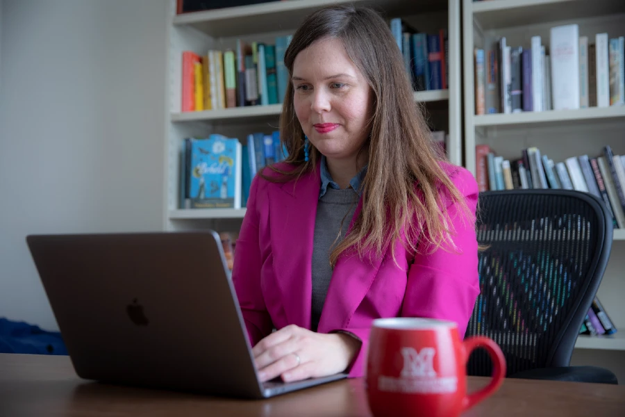 female student in hot pink blazer working at laptop with Miami University coffee mug sitting to her side on desk
