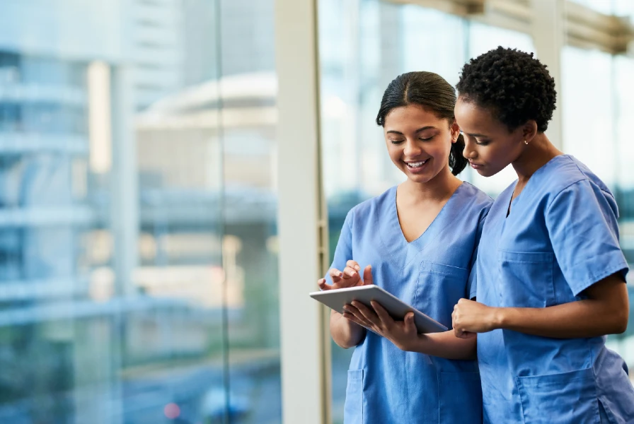 two nurses standing together wearing blue scrubs and looking at a chart