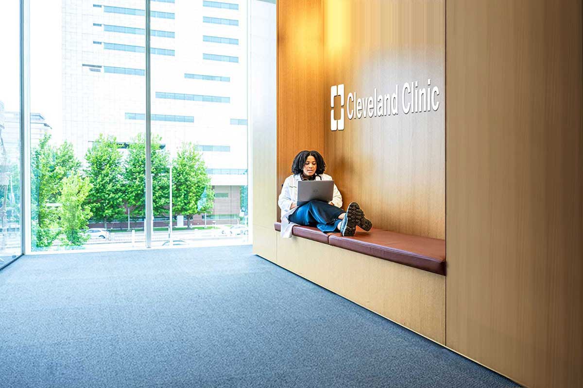 Woman sits with a laptop on a built-in bench in a wood-paneled Cleveland Clinic lobby.