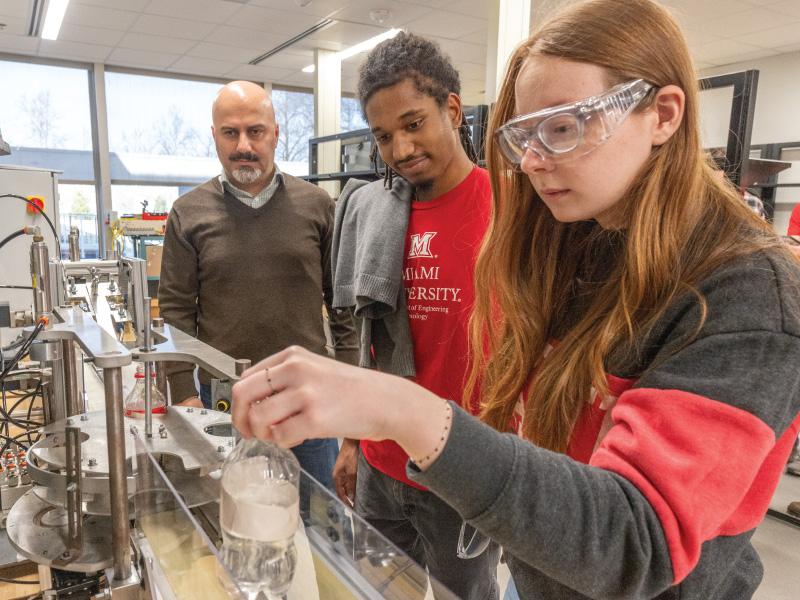 2 students and their professor working with a water bottle and a piece of engineering equipment.