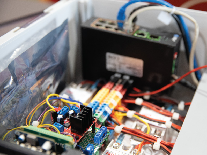 Inside an open equipment cabinet showing a red circuit board, power supply, and colorful wiring for a control system behind clear panels