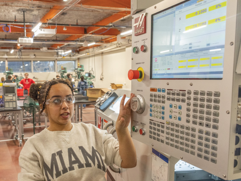Young woman wearing safety glasses operates a Haas CNC machine in a workshop l.